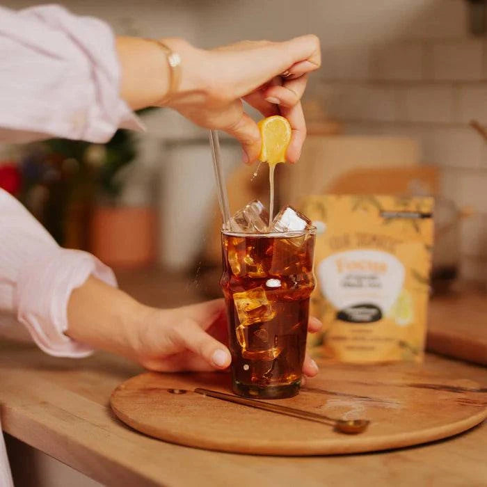 Four Sigmatic Organic Focus Black Tea in a glass with ice, showcasing the brewed tea and fresh lemon slices on a wooden table.