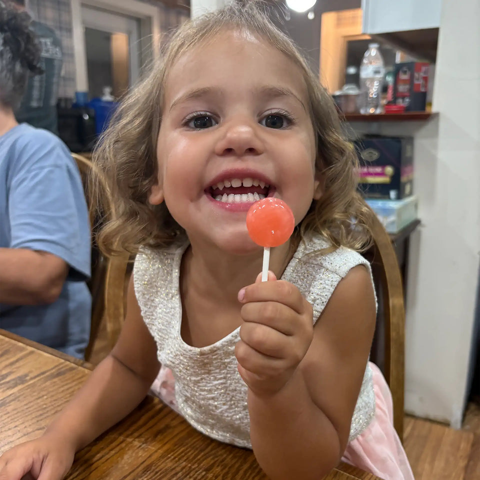 Girl smiling while holding assorted fruit-flavored Zollipops sugar-free lollipops in a 147g pack by Organax Ltd.
