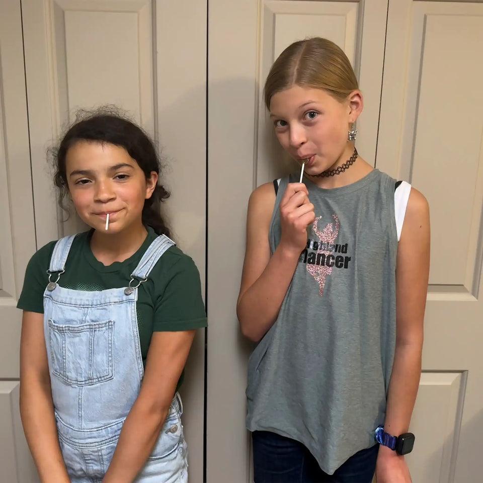 Girls holding Zollipops Elderberry sugar-free lollipops with vitamin C and zinc, in a 227g package, from Organax Ltd.