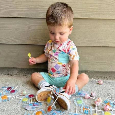 Toddler surrounded by Zollipops® Sugar Free Pineapple Lollipops, 3.1oz, in colorful packaging, promoting healthy candy options.