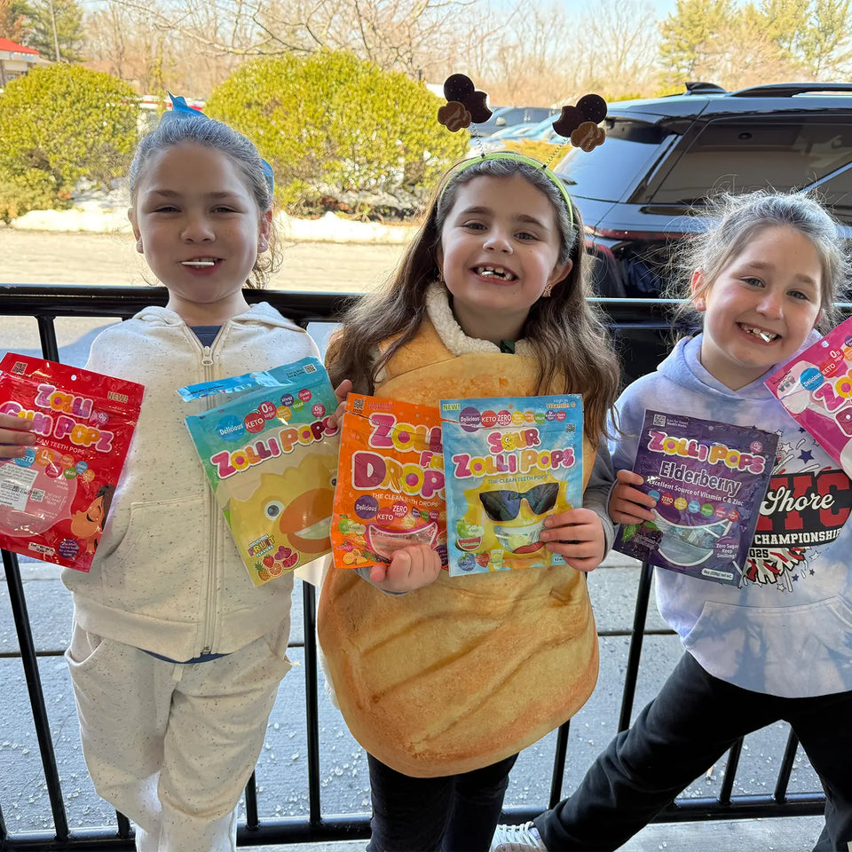 Girls outdoors holding Zollipops Elderberry sugar-free lollipops with Vitamin C and Zinc, showing the colorful packaging.